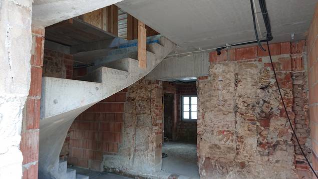 Im Eingang ist die neue Treppe wie auch eine Mischung aus Bestandsmauern und neuen Wänden zu sehen.